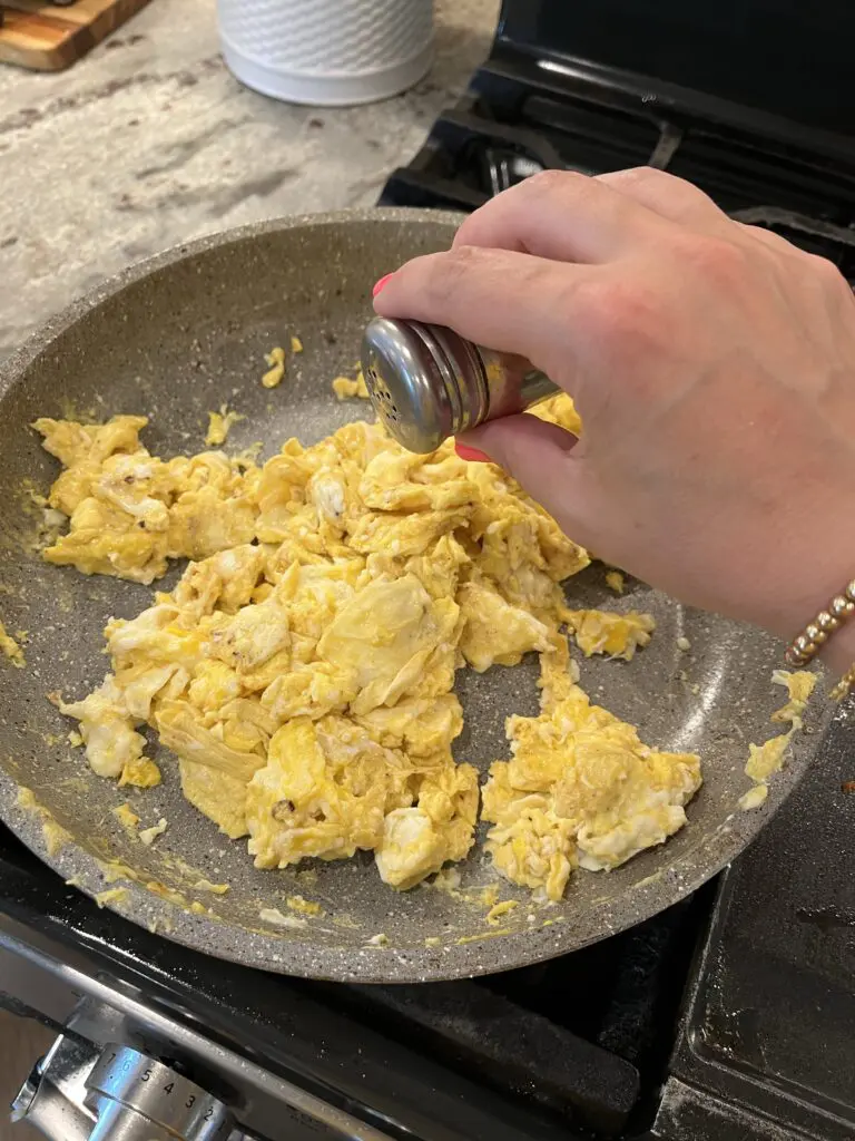 adding salt and pepper to the scrambled eggs
