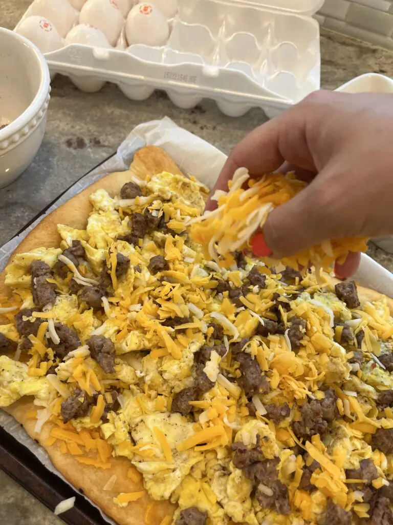 adding cheese to the breakfast pizza