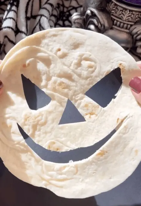 cut jack o lantern face out of a tortilla