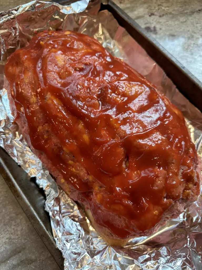 uncooked bacon cheeseburger meatloaf on baking sheet glazed with ketchup