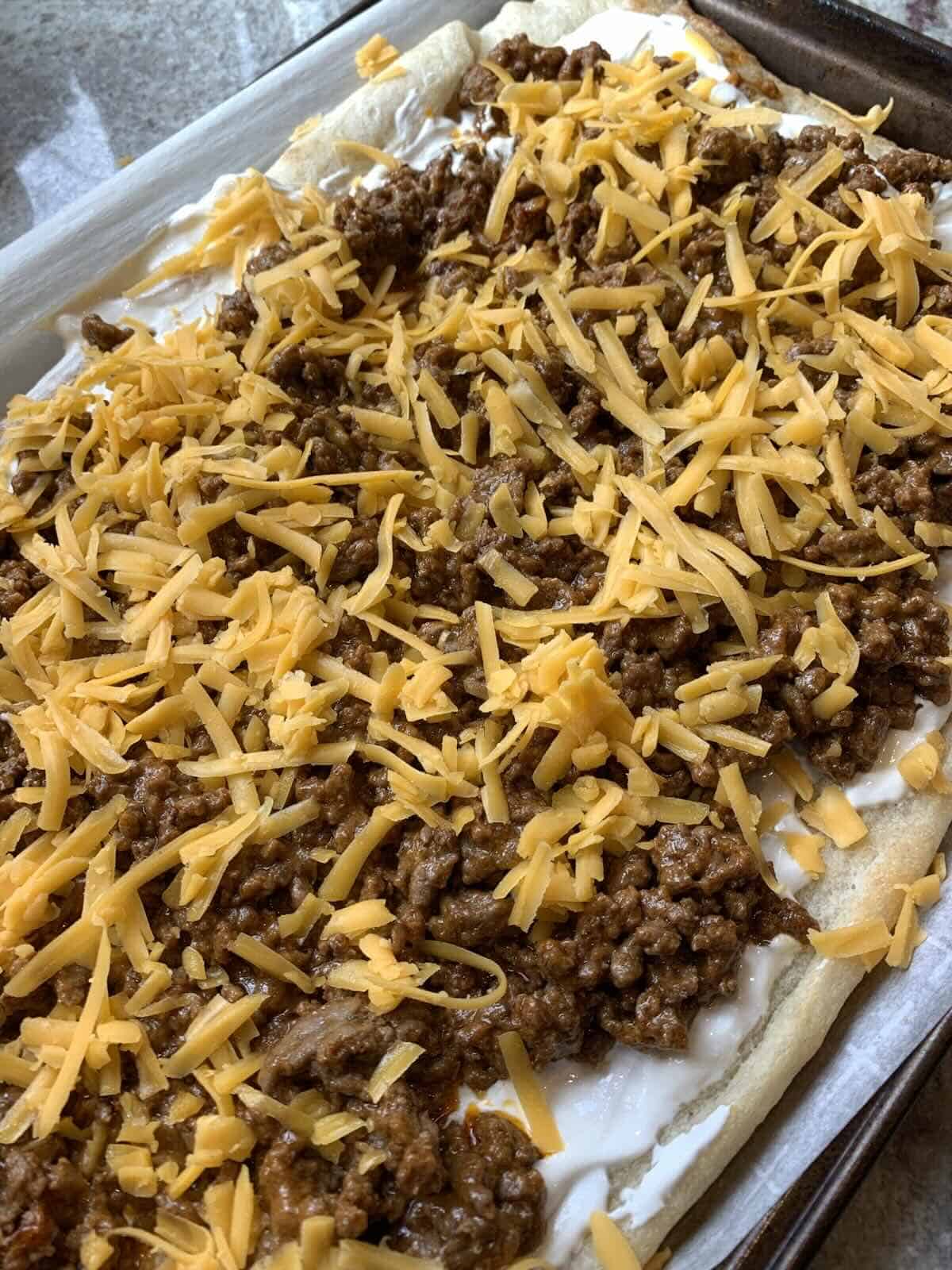 shredded cheddar cheese over taco seasoned ground beef on prepeard pizza dough
