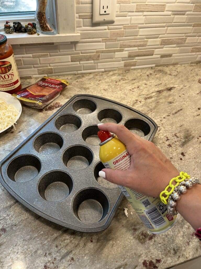 spraying muffin tin with cooking spray