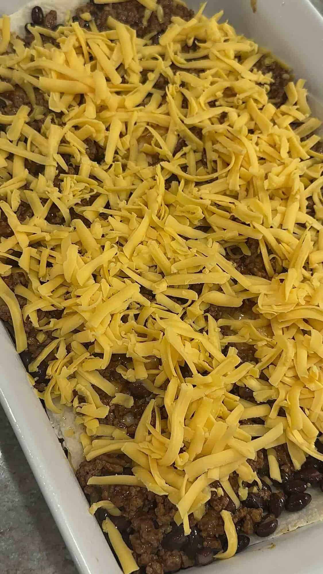 tortillas, seasoned ground beef, beans and cheese in a baking dish.