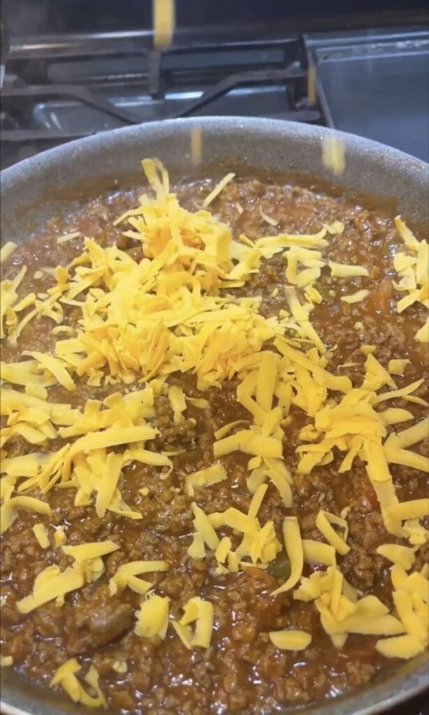shredded cheddar cheese on skillet nachos on stove