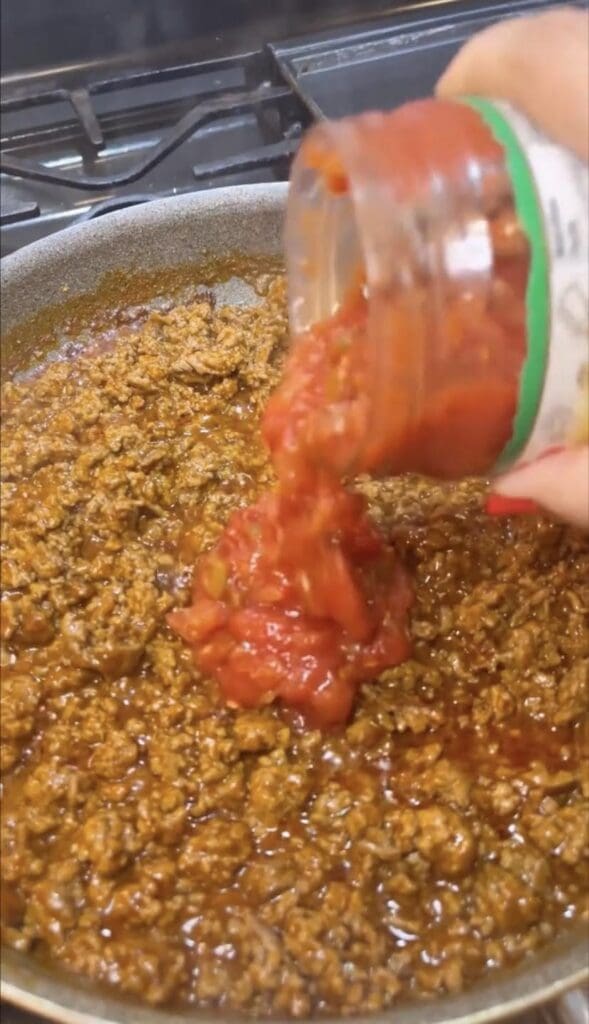 pouring salsa on ground beef on stove