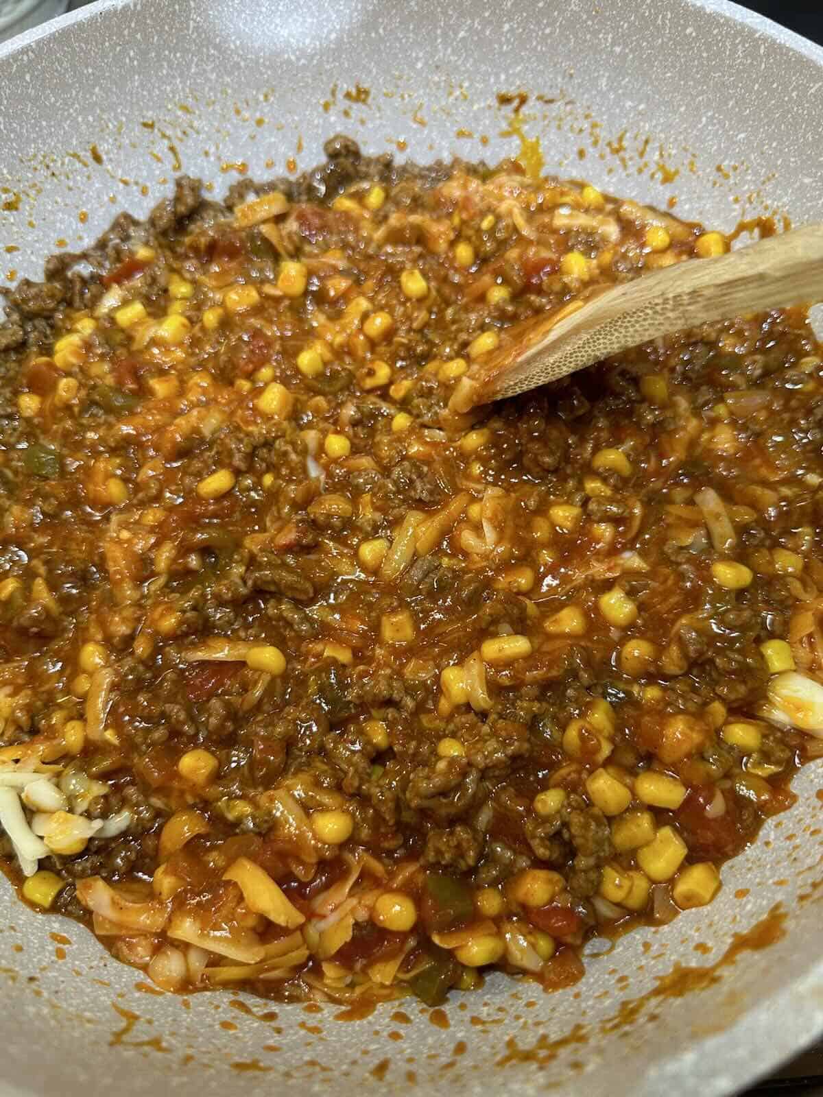 taco seasoned ground beef with corn beans and cheese in skillet