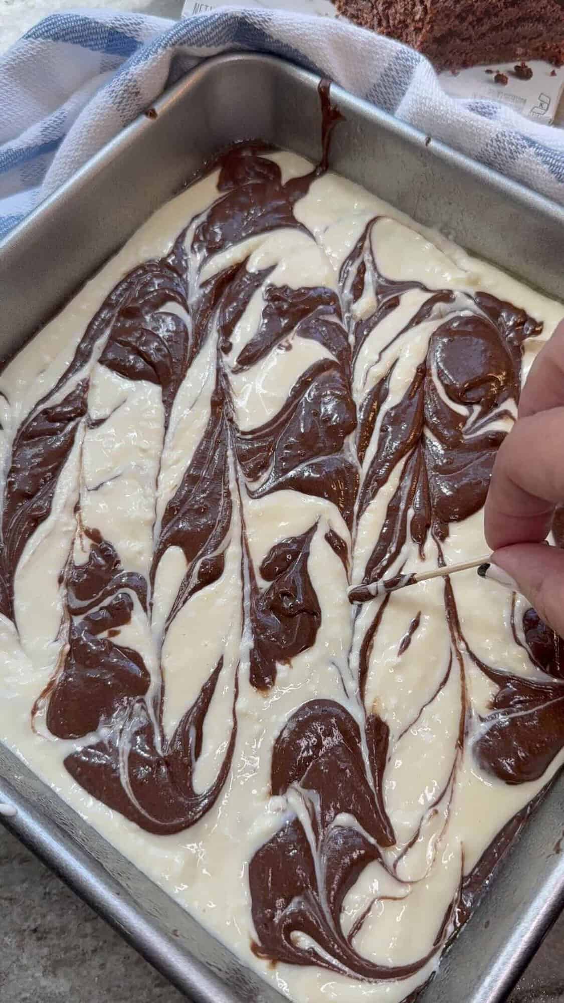 brownie and cheesecake mixture swirling in baking dish