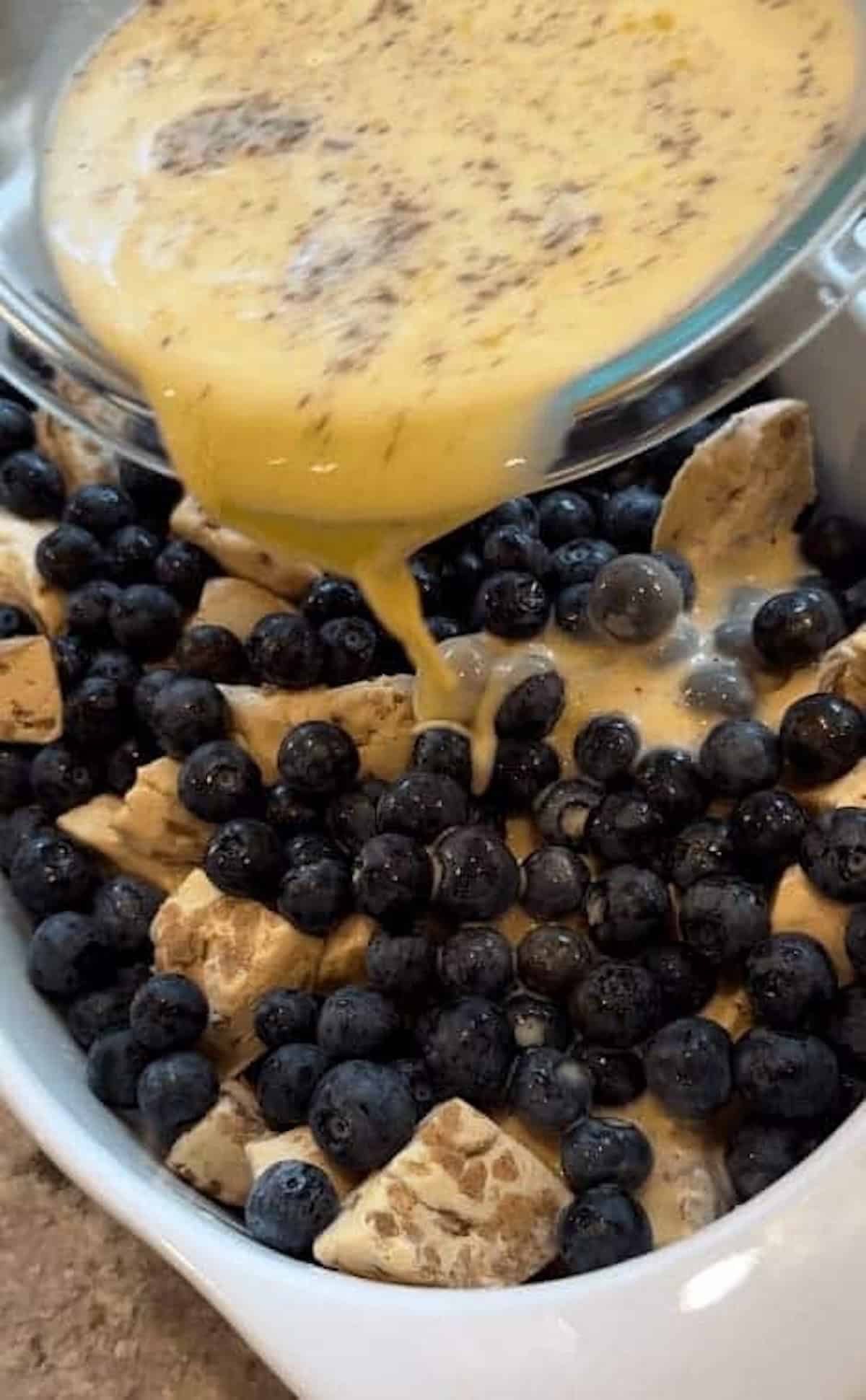custard being poured over blueberry casserole