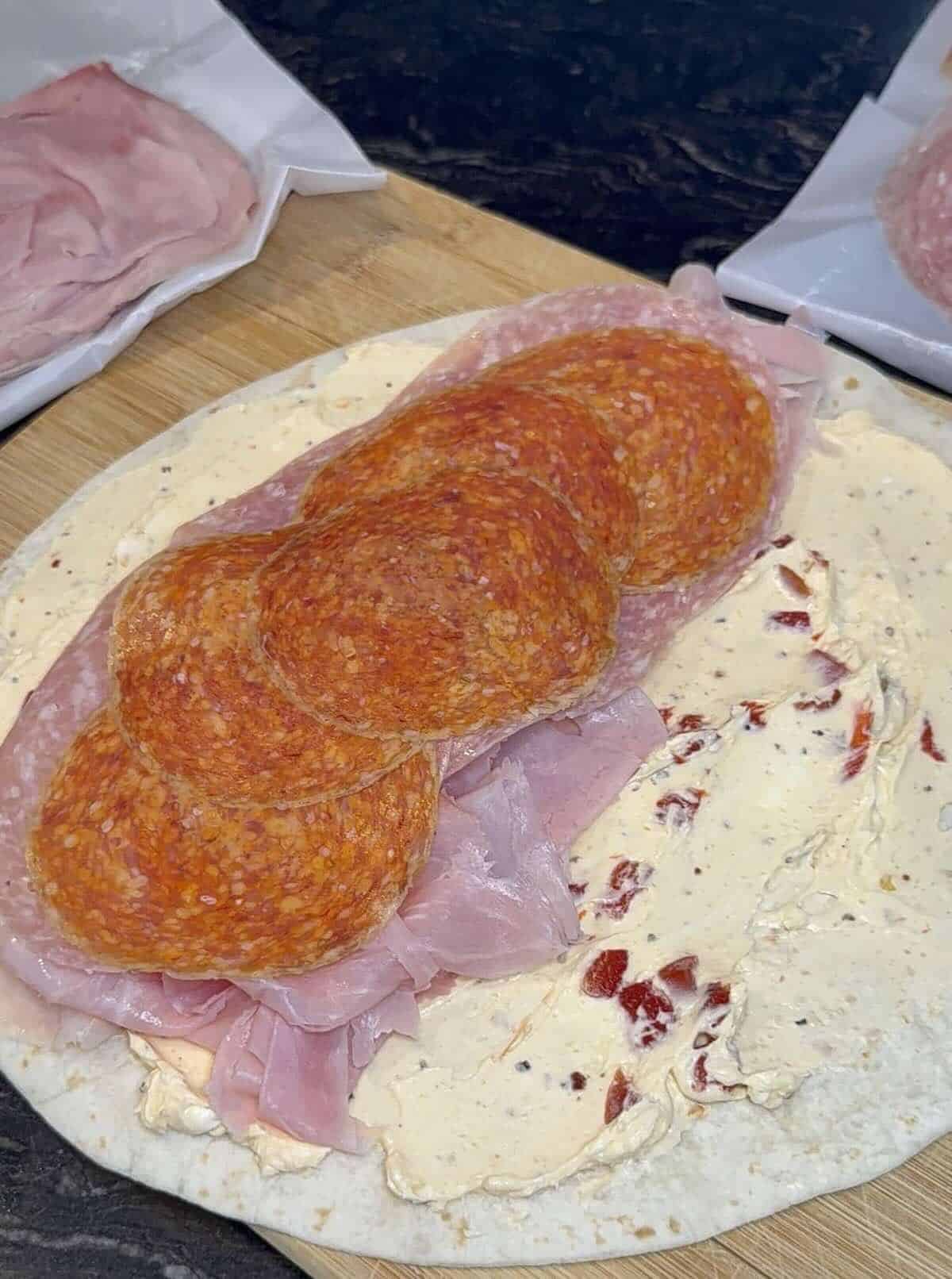 cold cuts on top of cream cheese on a large tortilla